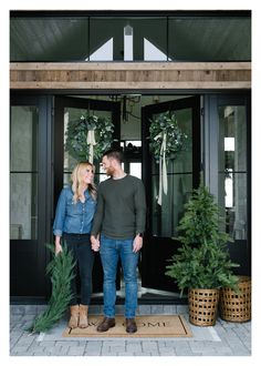 a man and woman standing in front of a black door with christmas wreaths on it