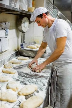 a man is kneading dough on a counter in a kitchen with lots of uncooked cookies