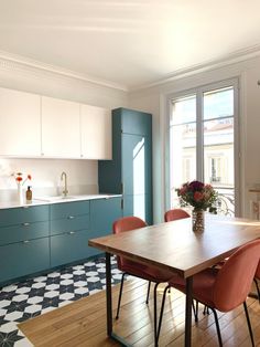 a kitchen with blue cabinets and wooden table surrounded by red chairs in front of an open window