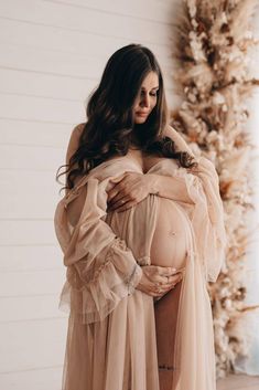 a pregnant woman wearing a dress standing in front of a christmas tree with her hands on her stomach