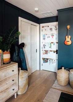 a room with blue walls and wooden floors, two baskets on the floor and a guitar hanging on the wall