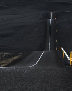 an empty road with yellow barriers on both sides and black hills in the back ground