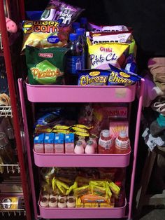 a pink cart filled with lots of food next to a shelf full of snacks and condiments