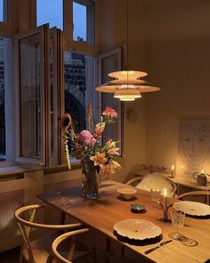 a dining room table with flowers in a vase and candles on the table next to it