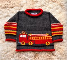 a sweater with a firetruck on it is laying on a white furnishing