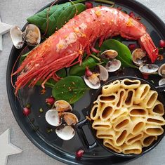 a black plate topped with pasta and lobster next to other food on top of it