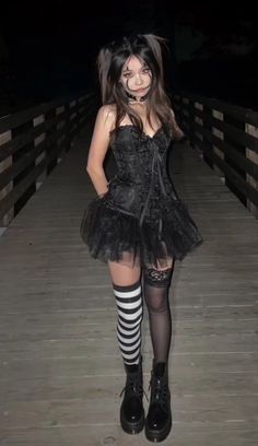 a woman dressed in black and white is posing for the camera on a wooden bridge