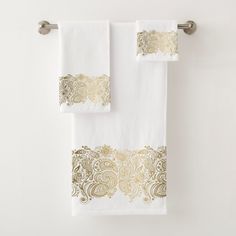 two white and gold towels hanging on a towel rack next to a toilet paper roll