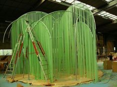 a large green structure with several ladders on it's sides in a warehouse