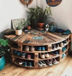 a round wooden table with several pairs of shoes on it and plants in the corner