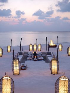 an outdoor dining area on the beach with lanterns lit up at night and water in the background