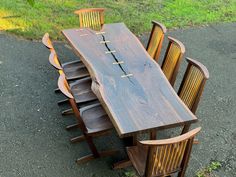 a wooden table with chairs around it in the middle of some grass and dirt area