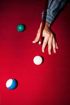 a person is reaching for balls on a red surface with pool cues in the foreground