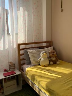 a small child's bedroom with yellow bedding and stuffed animals on the bed