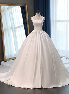 a white wedding dress on display in front of a mirror with blue drapes behind it