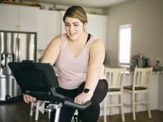 a woman is on a stationary bike in the kitchen while looking at her laptop computer