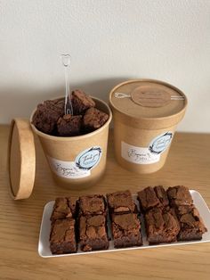 some brownies and ice cream are on a wooden table next to two containers with spoons