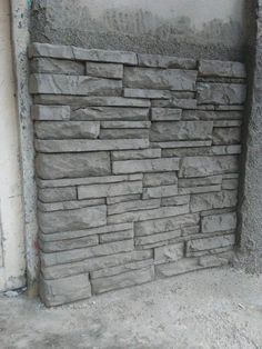 a stone wall in the corner of a room with cement walls and flooring on it