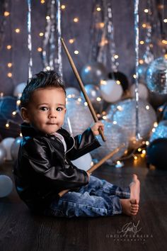 a young boy sitting on the floor with a broom in his hand and christmas decorations behind him