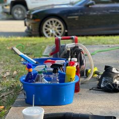 a blue bucket filled with cleaning supplies on the side of a road next to a car