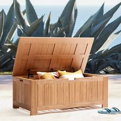 an open wooden box sitting on top of a sandy beach next to the ocean and plants