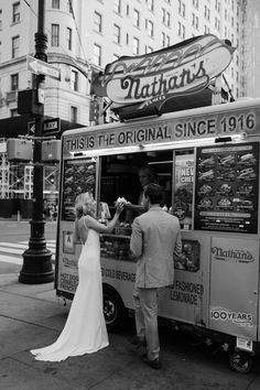 a man and woman are getting food from a vending truck on the sidewalk in front of a tall building