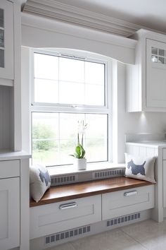 a white kitchen with a window seat and wooden counter top, along with cabinetry