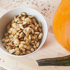 a white bowl filled with nuts next to an orange pumpkin