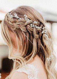 a woman with long blonde hair wearing a braid and flowers in her hair is seen from the back