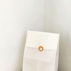 a white paper bag with an orange button on it sitting on a wooden floor next to a wall