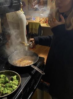 a woman is cooking broccoli in a wok on the stove with steam rising from it