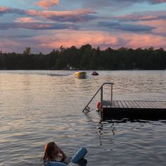 a person floating in the water near a dock with boats and people on it at sunset