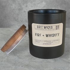 a black candle with a label on it next to a wooden sticker that says, get wicks and fire + whisky