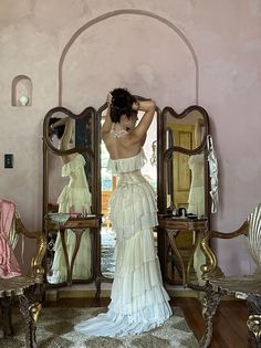 a woman standing in front of a mirror wearing a white dress with ruffles on it