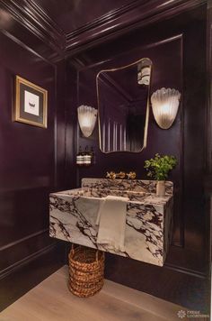 a bathroom with purple walls and marble counter top, gold framed mirror above the sink