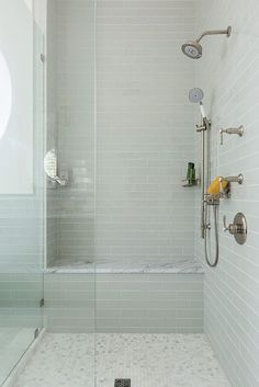 a walk in shower sitting next to a white tiled wall and floor with glass doors