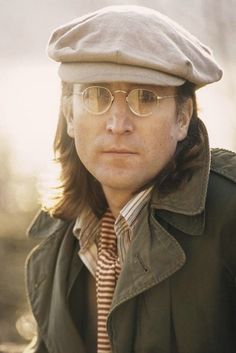 a man with long hair wearing glasses and a hat is looking at the camera while standing outside