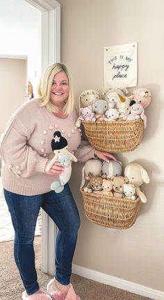 a woman standing next to a wall with stuffed animals in baskets on top of it