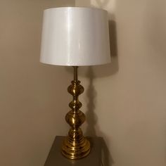 a gold lamp on a shelf with a white lampshade in front of it