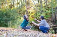 a man kneeling down next to a woman in the woods