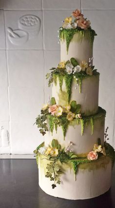 a three tiered cake with flowers and greenery on it