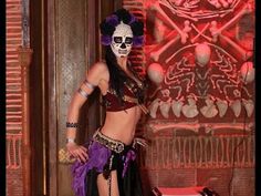 a woman in a costume standing next to a wall with skulls and bones on it