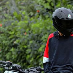 a person wearing a helmet and sitting on a motorbike in front of some trees