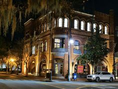 an old brick building lit up at night with street lights and cars parked in front