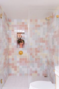 a white toilet sitting next to a walk in shower under a bathroom mirror on top of a tiled wall