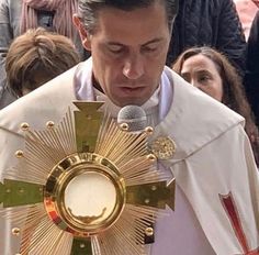 a man in a priest's outfit is holding a microphone and looking down at the cross