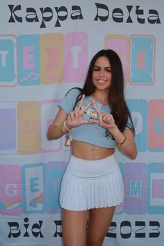 a woman in a blue shirt and white skirt posing for the camera with her peace sign