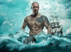 a man standing in the ocean with an old ship behind him and tattoos on his chest