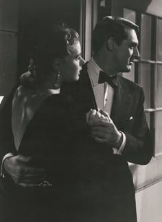 an old black and white photo of a man in a tuxedo hugging a woman