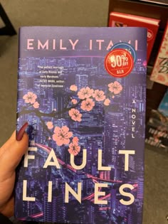 a person holding up a book in front of some bookshelves with the title fault lines written on it